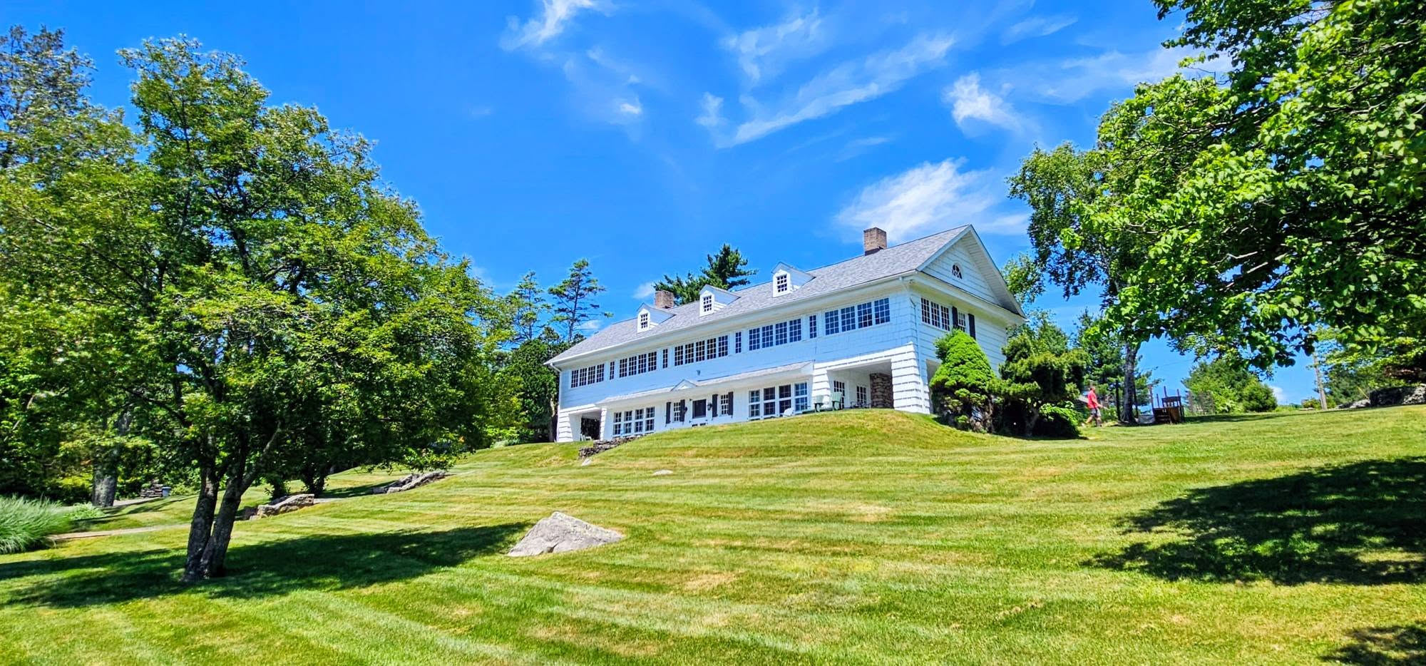 Elegant white two-story colonial home with a fresh exterior paint finish, set on a landscaped hillside lawn